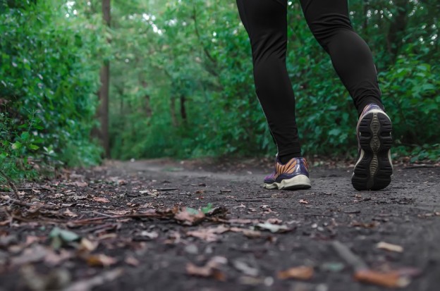 Sports shoes walking or jogging on green grass man runner cross country running on trail in summer forest. Athlete male training and doing workout outdoors in nature. Jogging workout fitness concept.